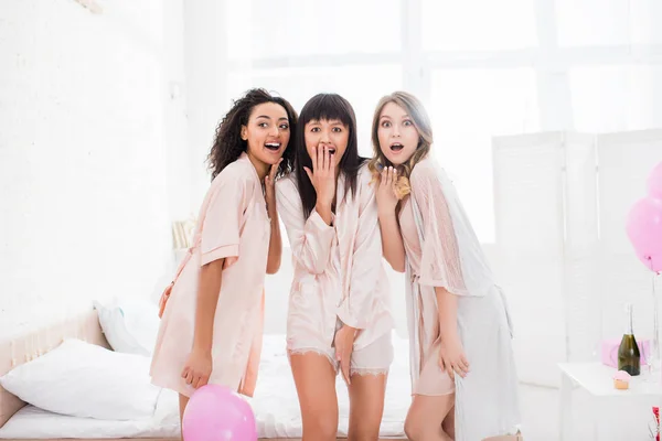 Shocked multicultural girls in nightwear in bedroom with pink balloons — Stock Photo