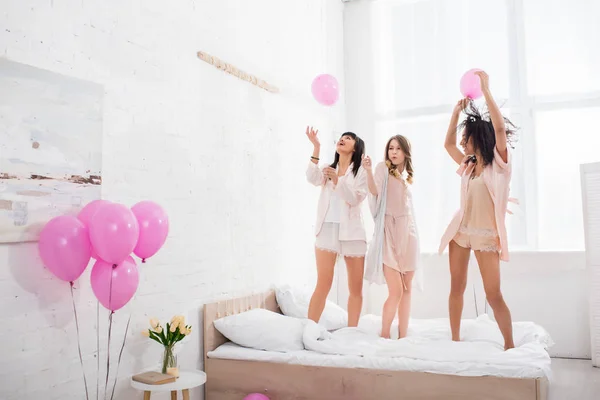 Attractive multicultural girls having fun with pink balloons in bedroom — Stock Photo