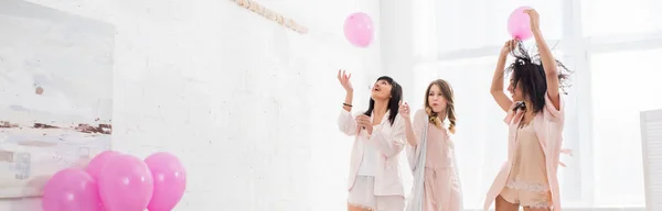 Plano panorámico de chicas alegres multiculturales divirtiéndose con globos rosados en despedida de soltera - foto de stock