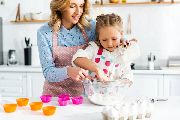 Beautiful mother and cute daughter sifting flour through sieve into bowl — Stock Photo