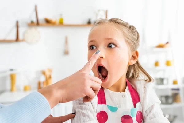 Mère toucher le nez de fille surprise pendant la cuisson dans la cuisine — Photo de stock