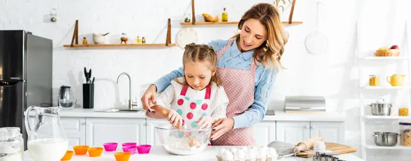 Hermosa atractiva madre de pie detrás de linda hija mientras amasa la masa, tiro panorámico - foto de stock