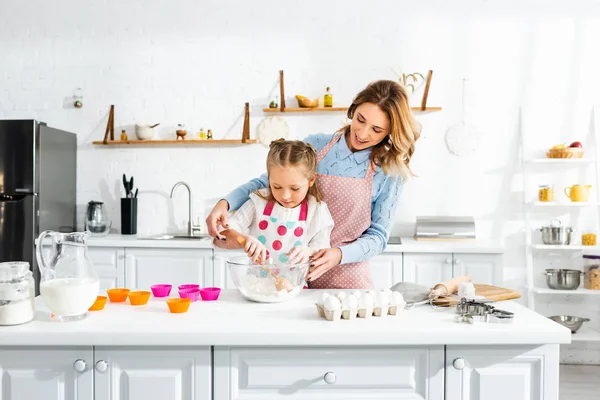 Красивая привлекательная мать, стоящая позади милой дочери, смешивая тесто — стоковое фото