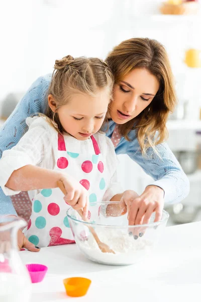 Focus selettivo di bella madre attraente e figlia carina concentrandosi sulla pasta impastare per cupcakes in cucina — Foto stock