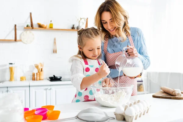 Selektiver Fokus der Tochter beim Kneten von Teig, während die Mutter zu Hause Milch aus dem Krug in die Schüssel gießt — Stockfoto