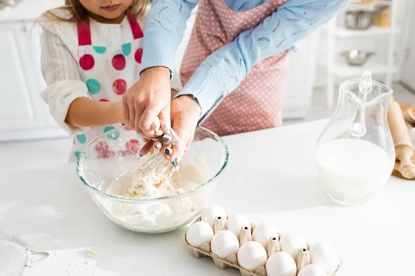 Cropped view of mother and daughter kneading dough together in bowl in kitchen — Stock Photo