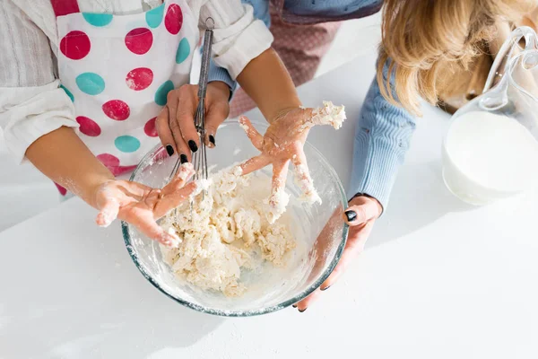 Vista ritagliata delle mani del bambino nella pasta vicino alla ciotola della madre — Foto stock