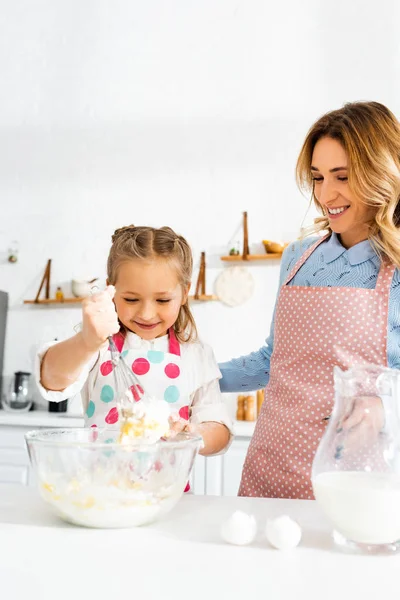 Selective focus of mother and daughter smiling and making dough for delicious cupcakes together — Stock Photo