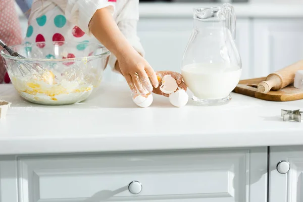 Vista recortada del niño rompiendo huevos en un tazón en la cocina - foto de stock