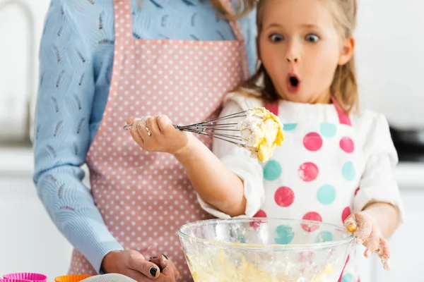 Selective focus of shocked and excited child looking at balloon whisk in dough above bowl — Stock Photo