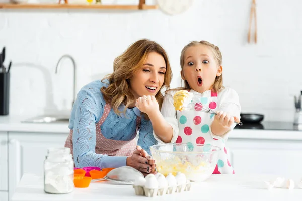 Mother and shocked, excited child looking at balloon whisk in dough above bowl — Stock Photo