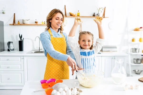 Sonriente madre e hija en delantales mezclando masa en la cocina - foto de stock