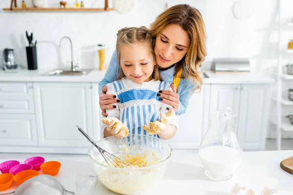 Sorridente madre abbracciando carina figlia durante la cottura pasta — Foto stock