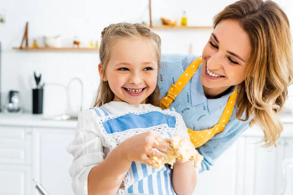 Smiling mother looking at cute daughter with dough on hands — Stock Photo