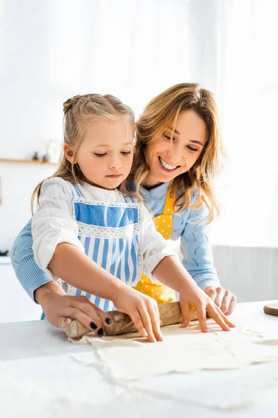 Улыбающаяся мать и милая дочь катят тесто на стол — стоковое фото