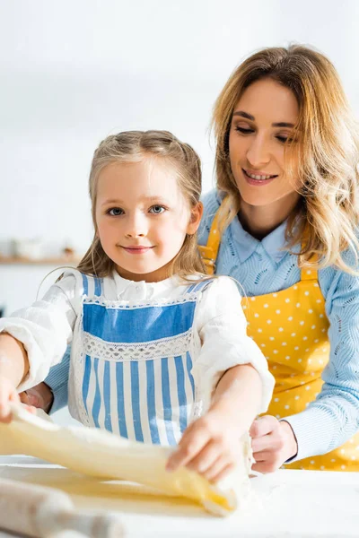 Mère souriante regardant fille mignonne avec de la pâte dans la cuisine — Photo de stock