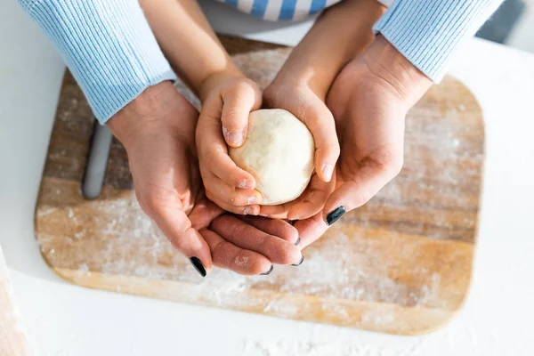 Vista recortada de madre e hija sosteniendo la masa en la cocina - foto de stock