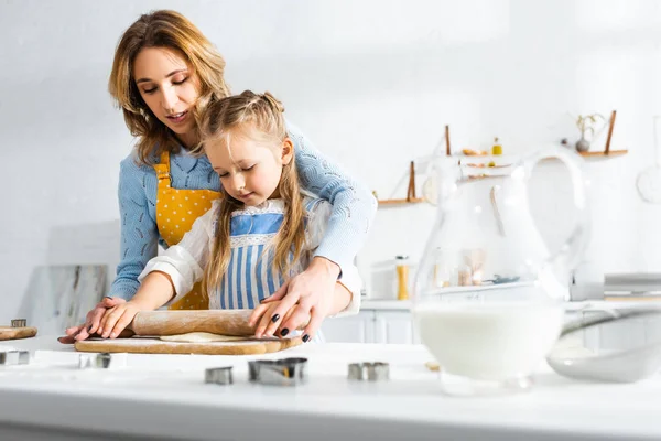 Mère attrayante et fille mignonne rouler la pâte sur la planche à découper — Photo de stock