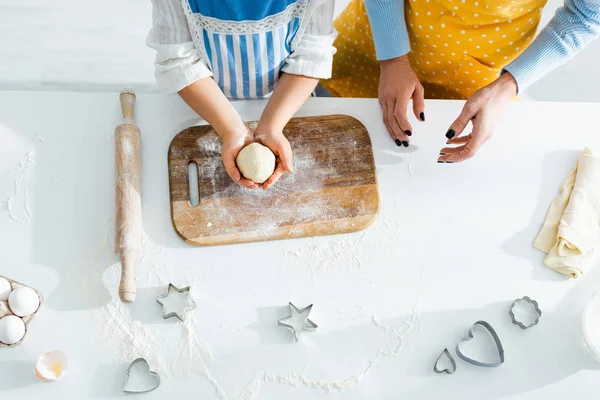 Vista recortada de madre e hija sosteniendo la masa en la cocina - foto de stock