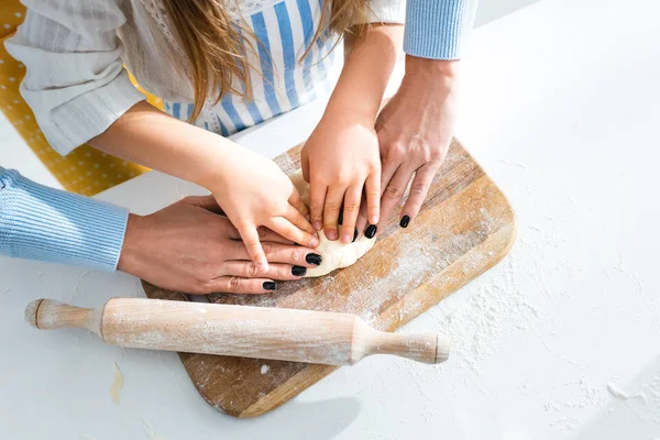 Vista recortada de la madre y la hija cocinar con masa en la tabla de cortar - foto de stock