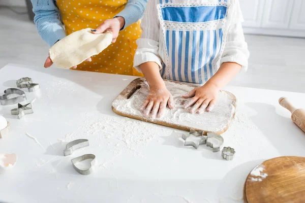 Cropped view of mother holding dough and daughter adding flour in kitchen — Stock Photo