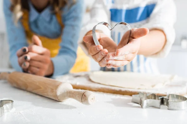 Cropped view of mother and daughter holding heart-shaped dough mold — Stock Photo