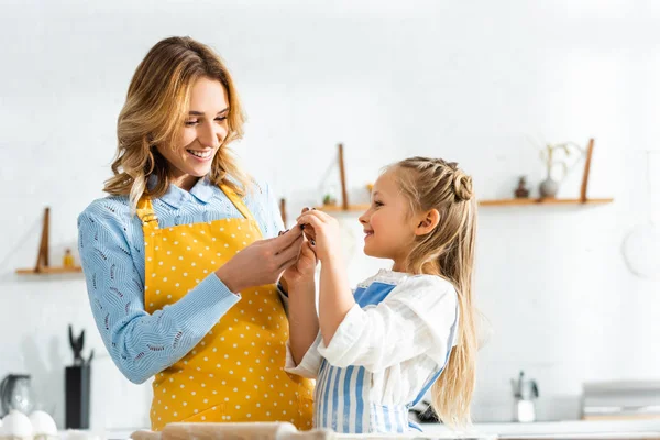 Sonriente madre y linda hija sosteniendo molde de masa en la cocina - foto de stock