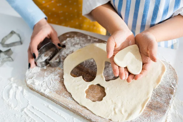 Cropped view of mother holding dough mold and daughter holding heart-shaped dough — Stock Photo
