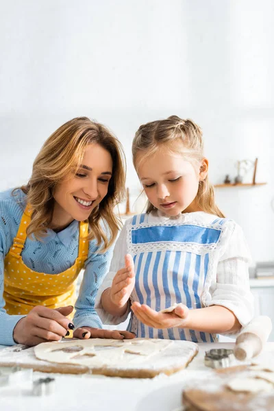 Smiling mother and cute daughter cooking cookies in kitchen — Stock Photo