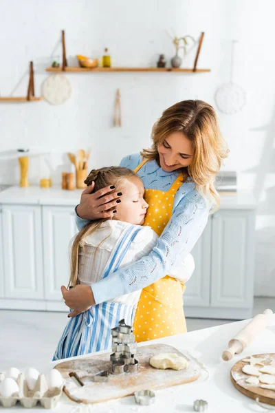 Smiling and attractive mother hugging cute daughter in kitchen — Stock Photo