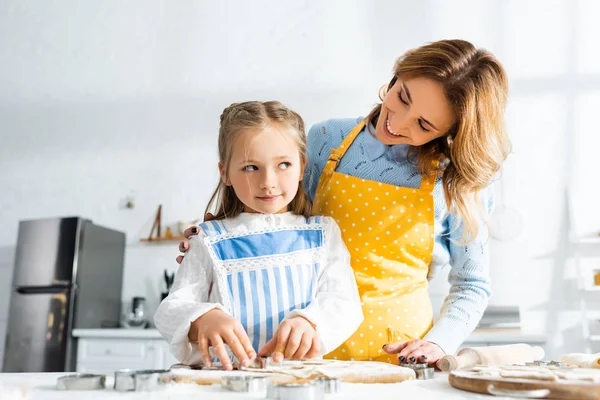 Sonriente madre y linda hija cocinar galletas en la cocina - foto de stock