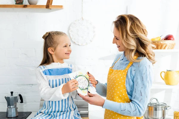 Hija presentando tarjeta con feliz día de las madres letras a la madre sonriente - foto de stock