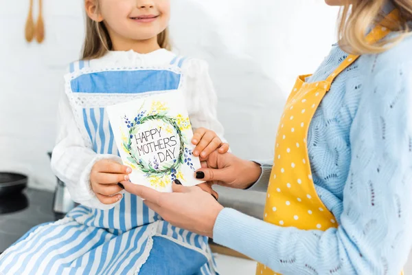 Vue recadrée de fille souriante présentant la carte avec le lettrage heureux de la fête des mères à la mère — Photo de stock