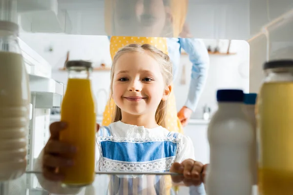 Messa a fuoco selettiva del bambino sorridente che prende il succo d'arancia dal frigorifero — Foto stock