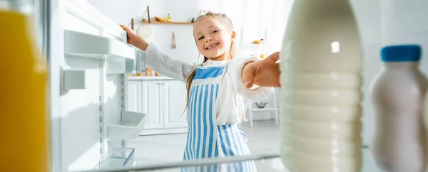 Colpo panoramico di bambino sorridente che prende la bottiglia con latte dal frigorifero — Foto stock