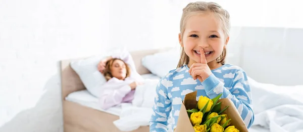 Panoramaaufnahme einer lächelnden Tochter, die shh zeigt und Blumenstrauß am Muttertag hält — Stockfoto