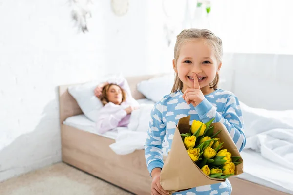 Foco seletivo de filha sorridente mostrando shh e segurando buquê no dia das mães — Fotografia de Stock