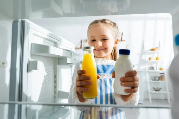 Enfoque selectivo del niño sonriente sosteniendo botellas con jugo de naranja y leche - foto de stock
