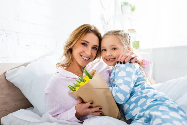 Улыбающаяся мать с букетом обнимает дочь в День матери — стоковое фото