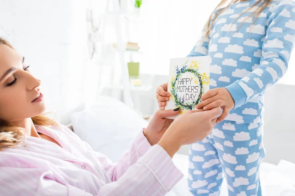 Cropped view of daughter presenting card with happy mothers day lettering to mother — Stock Photo