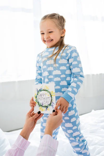 Smiling daughter presenting card with happy mothers day lettering to mother — Stock Photo