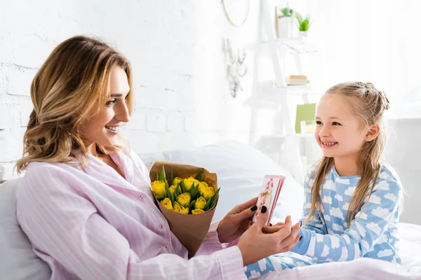 Sonriente hija dando tarjeta a la madre en el día internacional de las mujeres - foto de stock