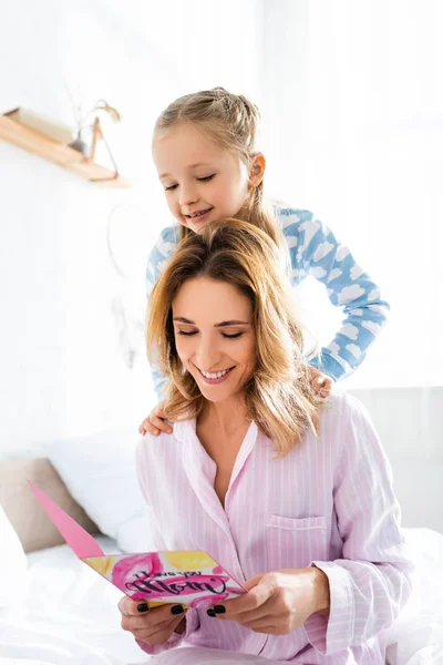 Sorrindo filha e mãe olhando para o cartão com eu amo você mãe lettering — Fotografia de Stock