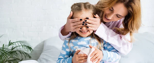 Panoramic shot of smiling mother obscuring face of daughter — Stock Photo