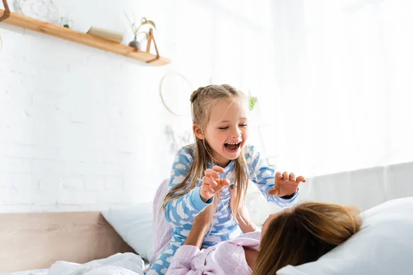 Mother holding and playing with smiling daughter on bed — Stock Photo