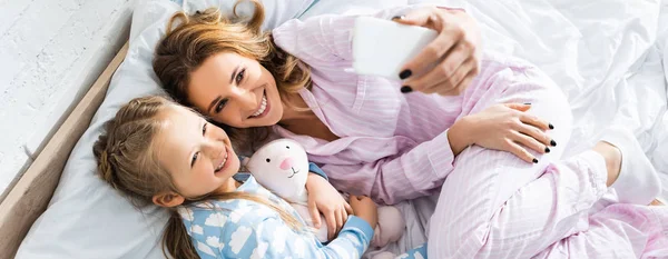 Plano panorámico de sonriente madre tomando selfie con linda hija - foto de stock