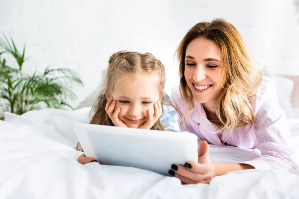 Улыбающиеся мать и дочь с помощью цифрового планшета в спальне — стоковое фото