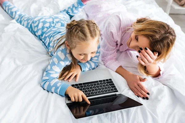 Vista aérea de la madre y la hija sonrientes apuntando con el dedo a la computadora portátil - foto de stock