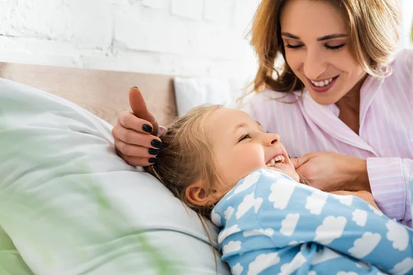 Селективное внимание улыбающейся матери, играющей с дочерью в спальне — стоковое фото