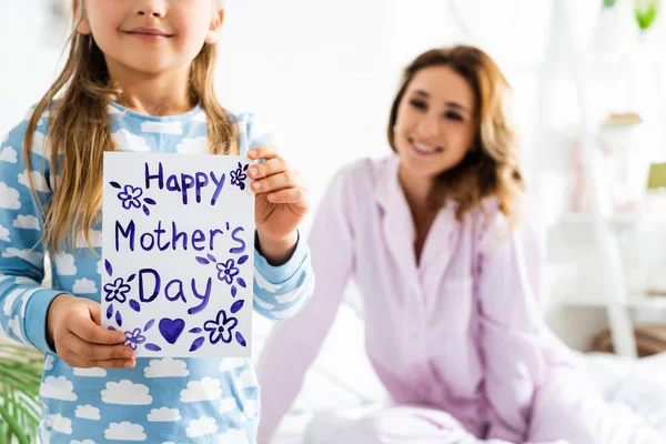 Vista ritagliata della figlia che tiene la carta con Happy Mothers Day lettering e madre sorridente — Foto stock